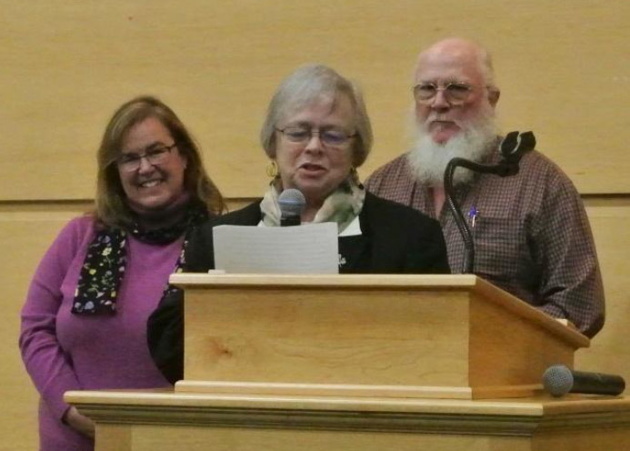 Three Clara Martin Center employees standing at a podium. One is reading a speech on a piece of paper with a microphone.
